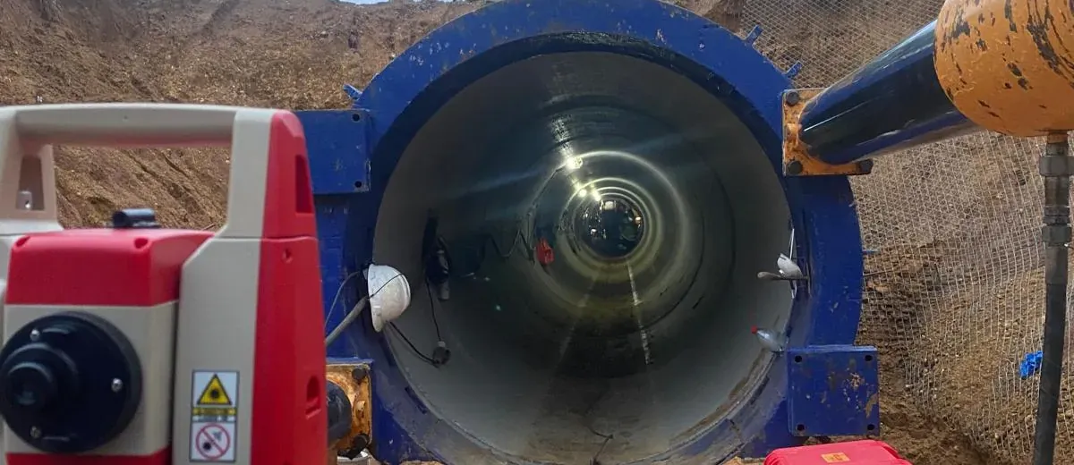 Estación total en primer plano frente a la boca de una tubería de gran diámetro en una obra